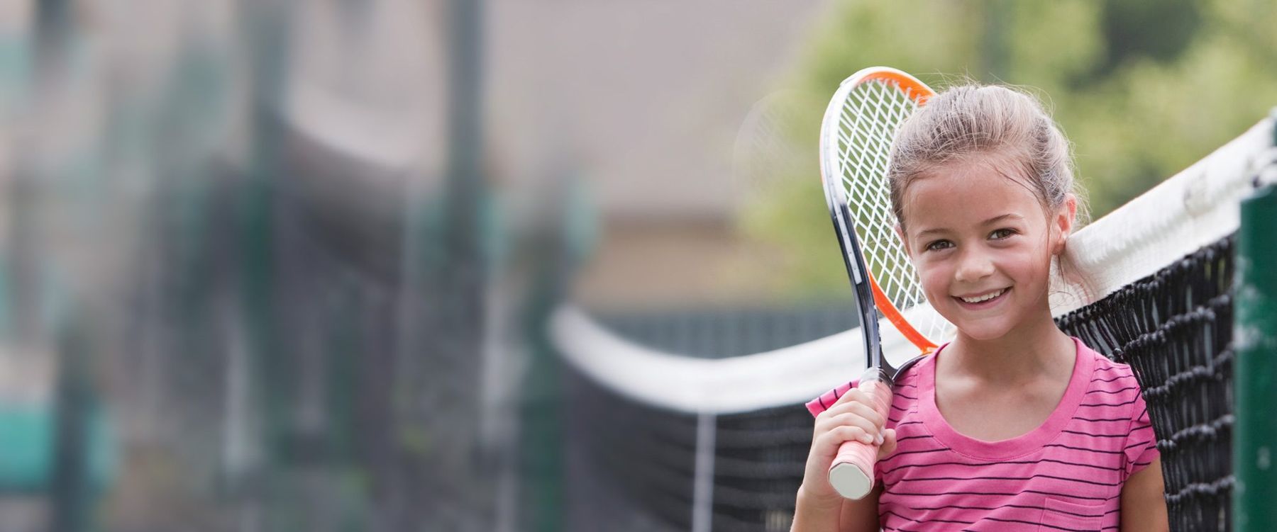 A smiling young girl with her racket by the net