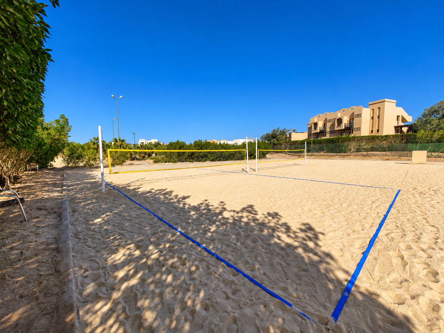 Sand courts for beach tennis, shaded by trees