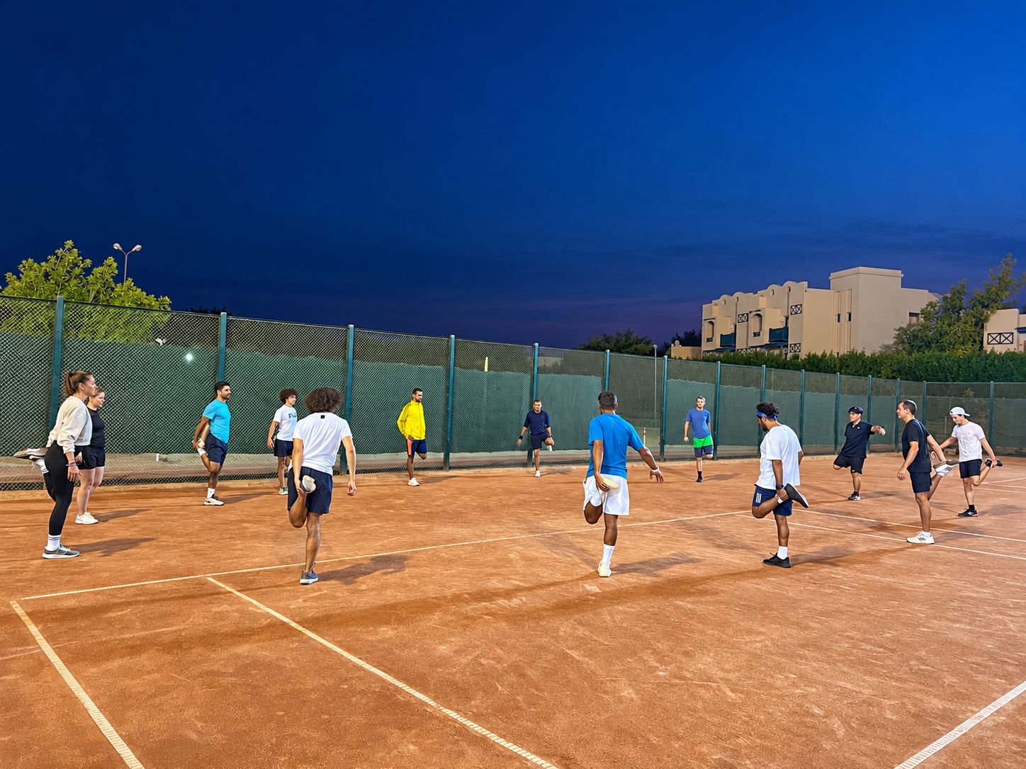 A group warming up together on the clay courts at dusk